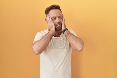 Téléchargez les photos : Homme d'âge moyen avec barbe debout sur fond jaune mains fatiguées couvrant le visage, la dépression et la tristesse, contrarié et irrité par le problème - en image libre de droit