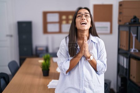 Photo for Young hispanic woman at the office begging and praying with hands together with hope expression on face very emotional and worried. begging. - Royalty Free Image