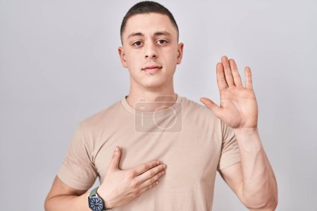 Téléchargez les photos : Young man standing over isolated background swearing with hand on chest and open palm, making a loyalty promise oath - en image libre de droit