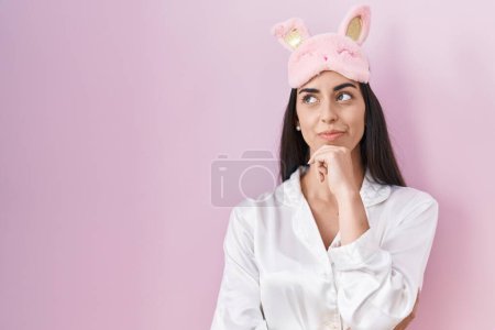 Photo for Young brunette woman wearing sleep mask and pajama serious face thinking about question with hand on chin, thoughtful about confusing idea - Royalty Free Image