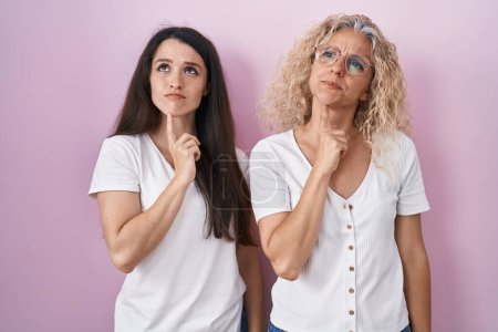 Photo for Mother and daughter standing together over pink background thinking concentrated about doubt with finger on chin and looking up wondering - Royalty Free Image