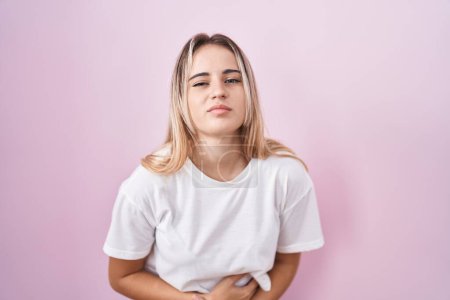 Téléchargez les photos : Young blonde woman standing over pink background with hand on stomach because indigestion, painful illness feeling unwell. ache concept. - en image libre de droit