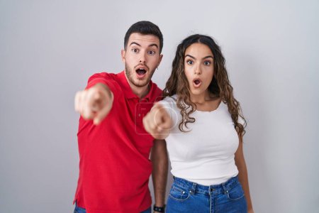 Téléchargez les photos : Young hispanic couple standing over isolated background pointing with finger surprised ahead, open mouth amazed expression, something on the front - en image libre de droit
