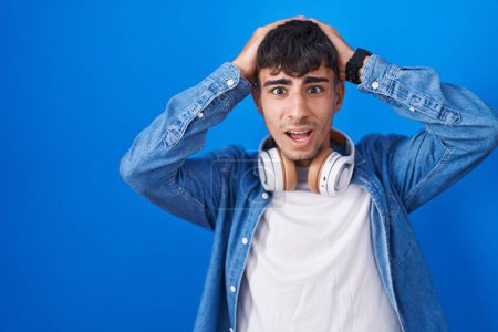 Photo for Young hispanic man standing over blue background crazy and scared with hands on head, afraid and surprised of shock with open mouth - Royalty Free Image