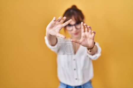 Téléchargez les photos : Jeune belle femme portant une chemise décontractée sur fond jaune faisant cadre en utilisant les mains paumes et les doigts, perspective de la caméra - en image libre de droit