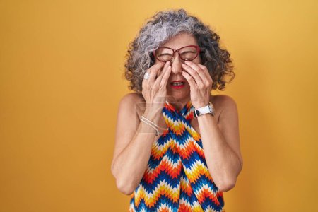 Téléchargez les photos : Femme d'âge moyen avec les cheveux gris debout sur fond jaune frottant les yeux pour la fatigue et les maux de tête, somnolent et l'expression fatiguée. problème de vision - en image libre de droit
