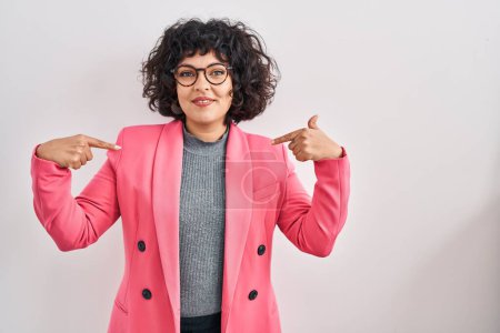 Foto de Hispanic woman with curly hair standing over isolated background looking confident with smile on face, pointing oneself with fingers proud and happy. - Imagen libre de derechos