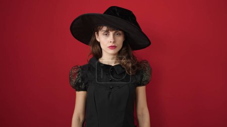 Téléchargez les photos : Jeune femme caucasienne regardant porter un costume de sorcière grave sur fond rouge isolé - en image libre de droit