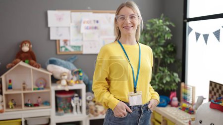 Téléchargez les photos : Jeune femme blonde travaillant comme professeur souriant heureux à la maternelle - en image libre de droit