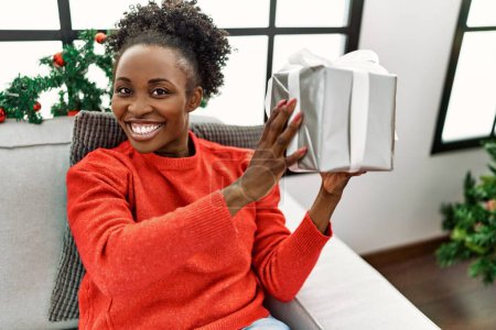 Foto de Mujer afroamericana sosteniendo regalo de Navidad sentada en sofá en casa - Imagen libre de derechos
