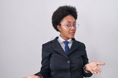 Foto de Beautiful african woman with curly hair wearing business jacket and glasses clueless and confused with open arms, no idea concept. - Imagen libre de derechos