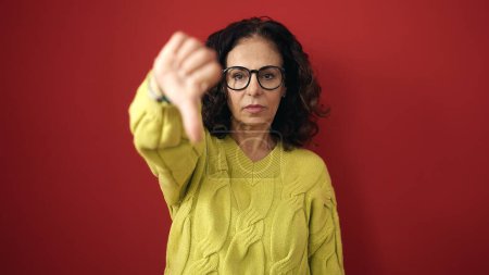 Photo for Middle age hispanic woman doing negative gesture with thumb down over isolated red background - Royalty Free Image