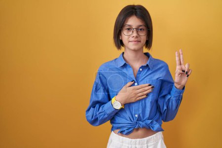 Photo for Young girl standing over yellow background smiling swearing with hand on chest and fingers up, making a loyalty promise oath - Royalty Free Image