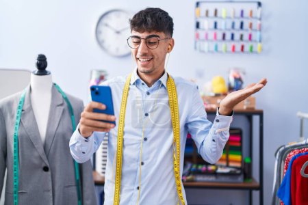 Photo for Young hispanic man dressmaker designer using smartphone celebrating achievement with happy smile and winner expression with raised hand - Royalty Free Image