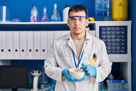 Photo for Young arab man working at scientist laboratory relaxed with serious expression on face. simple and natural looking at the camera. - Royalty Free Image