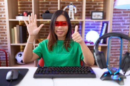 Foto de Mujer china de mediana edad con gafas de realidad virtual mostrando y apuntando hacia arriba con los dedos número seis mientras sonríe confiado y feliz. - Imagen libre de derechos