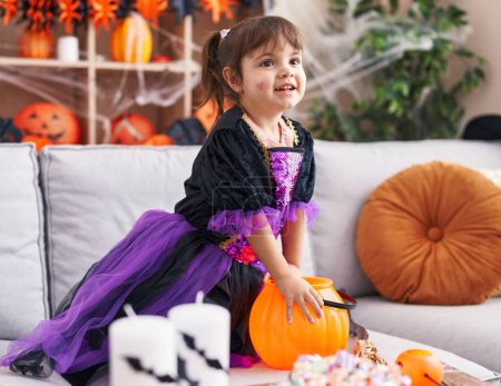 Téléchargez les photos : Adorable fille hispanique portant costume d'Halloween tenant des bonbons à la maison - en image libre de droit