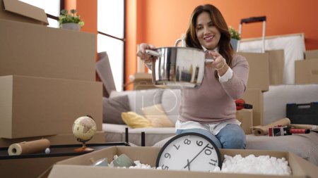 Photo for Young beautiful hispanic woman smiling confident unpacking cardboard box at new home - Royalty Free Image