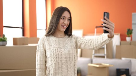 Photo for Young beautiful hispanic woman make selfie by smartphone standing at new home - Royalty Free Image