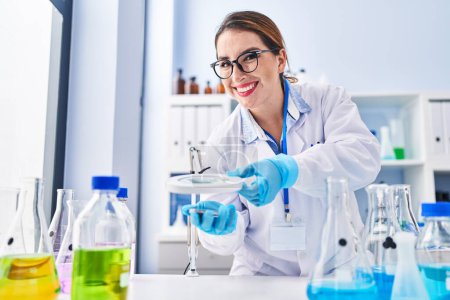 Photo for Young beautiful hispanic woman scientist smiling confident using magnifying glass at laboratory - Royalty Free Image