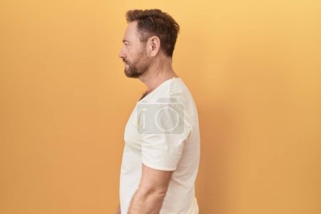 Photo for Middle age man with beard standing over yellow background looking to side, relax profile pose with natural face and confident smile. - Royalty Free Image