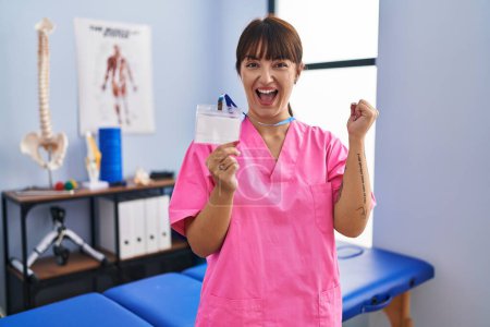 Photo for Young brunette woman working at rehabilitation clinic showing id screaming proud, celebrating victory and success very excited with raised arm - Royalty Free Image