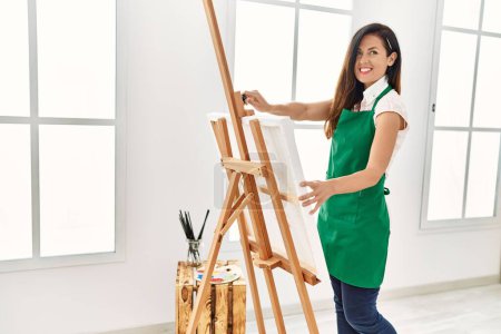 Foto de Mujer hispana de mediana edad sonriendo confiado dibujo de lienzo en el estudio de arte - Imagen libre de derechos