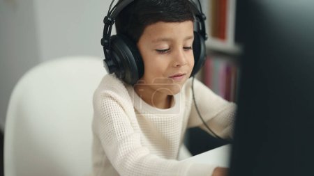 Téléchargez les photos : Adorable hispanic boy student using computer sitting on table at classroom - en image libre de droit