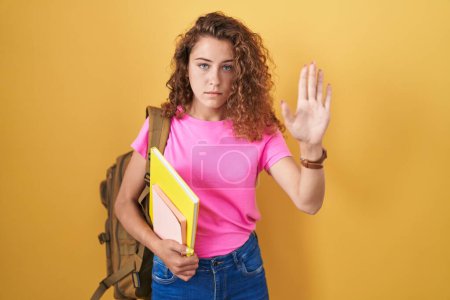 Photo for Young caucasian woman wearing student backpack and holding books doing stop sing with palm of the hand. warning expression with negative and serious gesture on the face. - Royalty Free Image