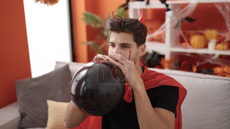 Téléchargez les photos : Jeune homme hispanique portant costume diable ballon gonflant à la maison - en image libre de droit