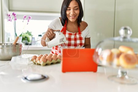 Photo for Hispanic brunette woman preparing cake looking at online recipe at the kitchen - Royalty Free Image