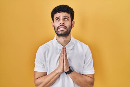 Photo for Arab man standing over yellow background begging and praying with hands together with hope expression on face very emotional and worried. begging. - Royalty Free Image