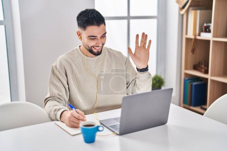 Téléchargez les photos : Jeune homme beau utilisant ordinateur portable faisant appel en ligne regardant positif et heureux debout et souriant avec un sourire confiant montrant les dents - en image libre de droit