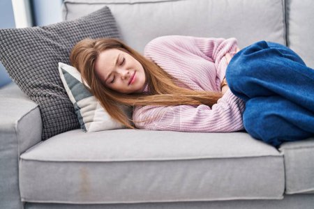 Téléchargez les photos : Young caucasian woman suffering for menstrual pain lying on sofa at home - en image libre de droit
