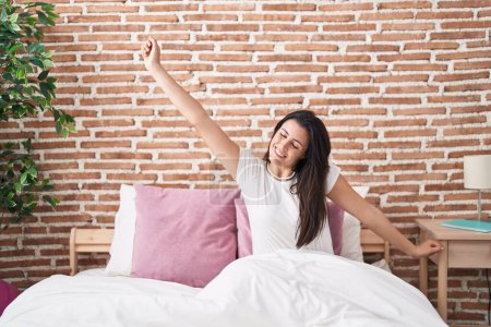 Foto de Joven hermosa mujer hispana despertando estirando los brazos en el dormitorio - Imagen libre de derechos