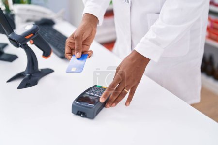 Photo for Middle age african american woman pharmacist using credit card and data phone at pharmacy - Royalty Free Image
