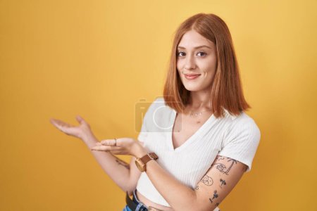 Téléchargez les photos : Jeune rousse femme debout sur fond jaune invitant à entrer souriant naturel avec la main ouverte - en image libre de droit
