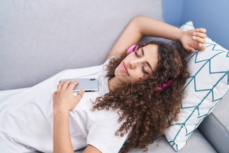Téléchargez les photos : Jeune belle femme hispanique écoutant de la musique dormir sur le canapé à la maison - en image libre de droit