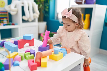 Foto de Adorable niño rubio jugando con bloques de construcción de pie en el jardín de infantes - Imagen libre de derechos