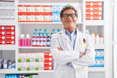 Téléchargez les photos : Middle age man pharmacist smiling confident standing with arms crossed gesture at pharmacy - en image libre de droit