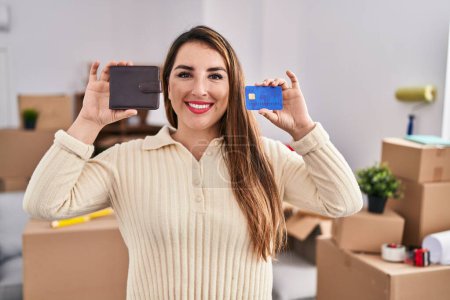 Photo for Young hispanic woman moving to a new home holding wallet and credit card smiling with a happy and cool smile on face. showing teeth. - Royalty Free Image