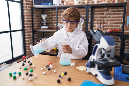 Photo for Adorable caucasian boy student pouring liquid on test tube at classroom - Royalty Free Image