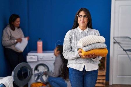 Photo for Three women doing laundry at home smiling looking to the side and staring away thinking. - Royalty Free Image