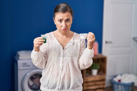 Foto de Middle age hispanic woman holding laundry detergent and laundry powder depressed and worry for distress, crying angry and afraid. sad expression. - Imagen libre de derechos