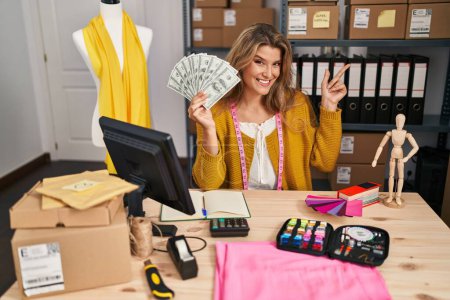 Photo for Young woman by manikin at small business holding money smiling happy pointing with hand and finger to the side - Royalty Free Image