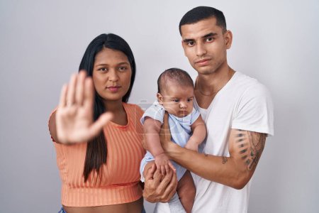 Photo for Young hispanic couple with baby standing together over isolated background doing stop sing with palm of the hand. warning expression with negative and serious gesture on the face. - Royalty Free Image