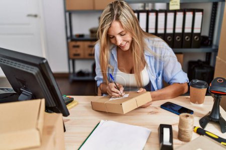 Téléchargez les photos : Jeune femme blonde ecommerce travailleur d'affaires écrit sur le paquet au bureau - en image libre de droit
