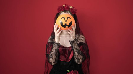 Photo for Young blonde woman wearing katrina costume holding halloween pumpkin basket over face over isolated red background - Royalty Free Image