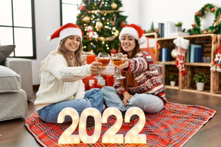 Téléchargez les photos : Femme couple toasting avec champagne pour la nouvelle année 2022 assis par arbre de Noël à la maison - en image libre de droit