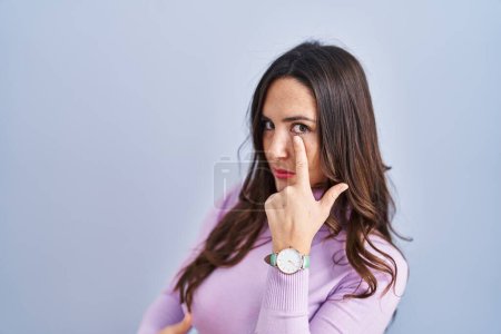 Téléchargez les photos : Jeune femme brune debout sur fond bleu pointant vers l'œil vous regardant geste, expression suspecte - en image libre de droit